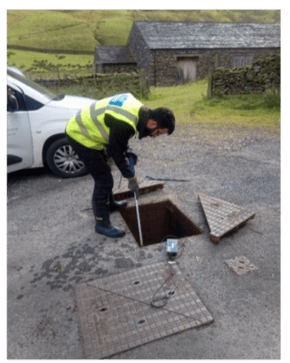 Engineer conducting a field test, using a tool to check a monitoring device inside an open manhole as part of the AMP7 hydraulic modeling project.