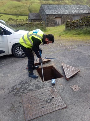 Engineer conducting a field test, using a tool to check a monitoring device inside an open manhole as part of the AMP7 hydraulic modeling project.
